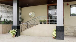 A staircase with metal railings leading to a building entrance, a stone wall with greenery, and a circular decorative element on the wall. - Super Collection O Ghodbunder Road (Mumbai)