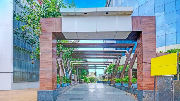 A modern building entrance with a covered walkway, potted plants, and a yellow signboard. - Deluxe With Twin Bed Sitabuldi Station (Nagpur)