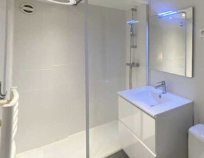 Un baño moderno con ducha envuelta en vidrio, un lavabo blanco y un espejo.