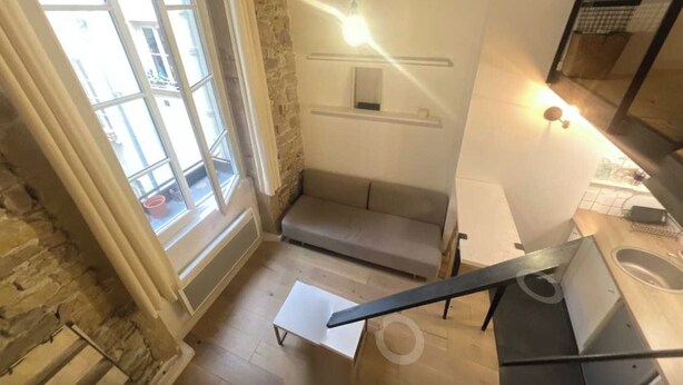 Quarto nos fundos com parede de pedra, um sofá cinza, uma mesa pequena e uma escada.