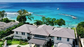 A coastal residential area with modern houses, clear blue waters, and a boat in the distance. - One Beachlands - by ZenBreak (Holetown)
