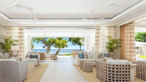 A spacious living area with a view of the ocean, furnished with sofas and chairs, and featuring ceiling fans. - One Beachlands - by ZenBreak (Holetown)