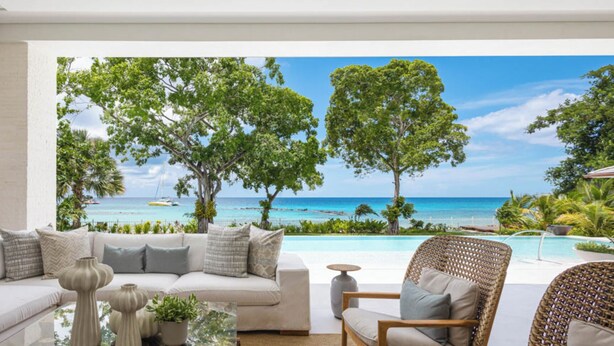 A modern living room with a sofa, armchairs, and a coffee table, overlooking a pool and a beach view. - One Beachlands - by ZenBreak (Holetown)