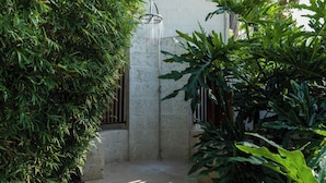 Zona de ducha de hormigón con grifo metálico, rodeada de exuberante follaje verde.