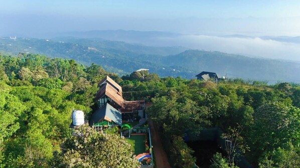 A house surrounded by lush greenery, with a clear view of distant mountains and a misty valley.