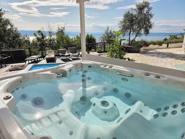 A hot tub with a view of the sea, surrounded by lounge chairs and a wooden deck.