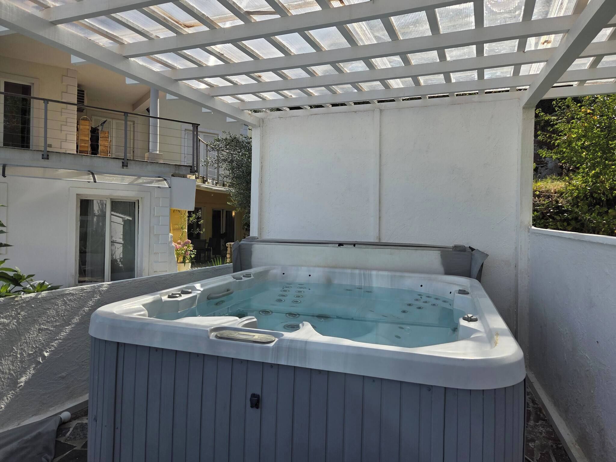 A hot tub under a pergola with a view of a residential building.
