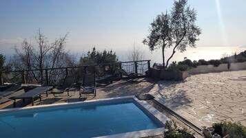 A pool area with lounge chairs and a view of the sea.