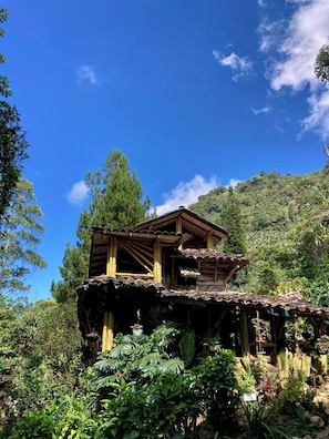 Eine rustikale Holzhütte mit geneigtem Dach, umgeben von üppigem Grün und Bäumen.