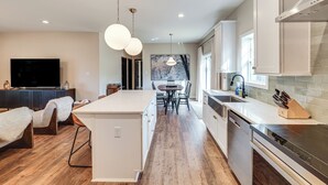 Une cuisine moderne dotée d’un îlot central, d’appareils électroménagers intégrés et de luminaires suspendus.