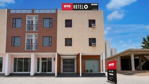 A hotel with a modern facade, featuring a mix of brick and beige exterior walls, large windows, and a prominent signboard advertising the hotel name and app booking option. - Deluxe Hotel Holiday Spot (Mohali)
