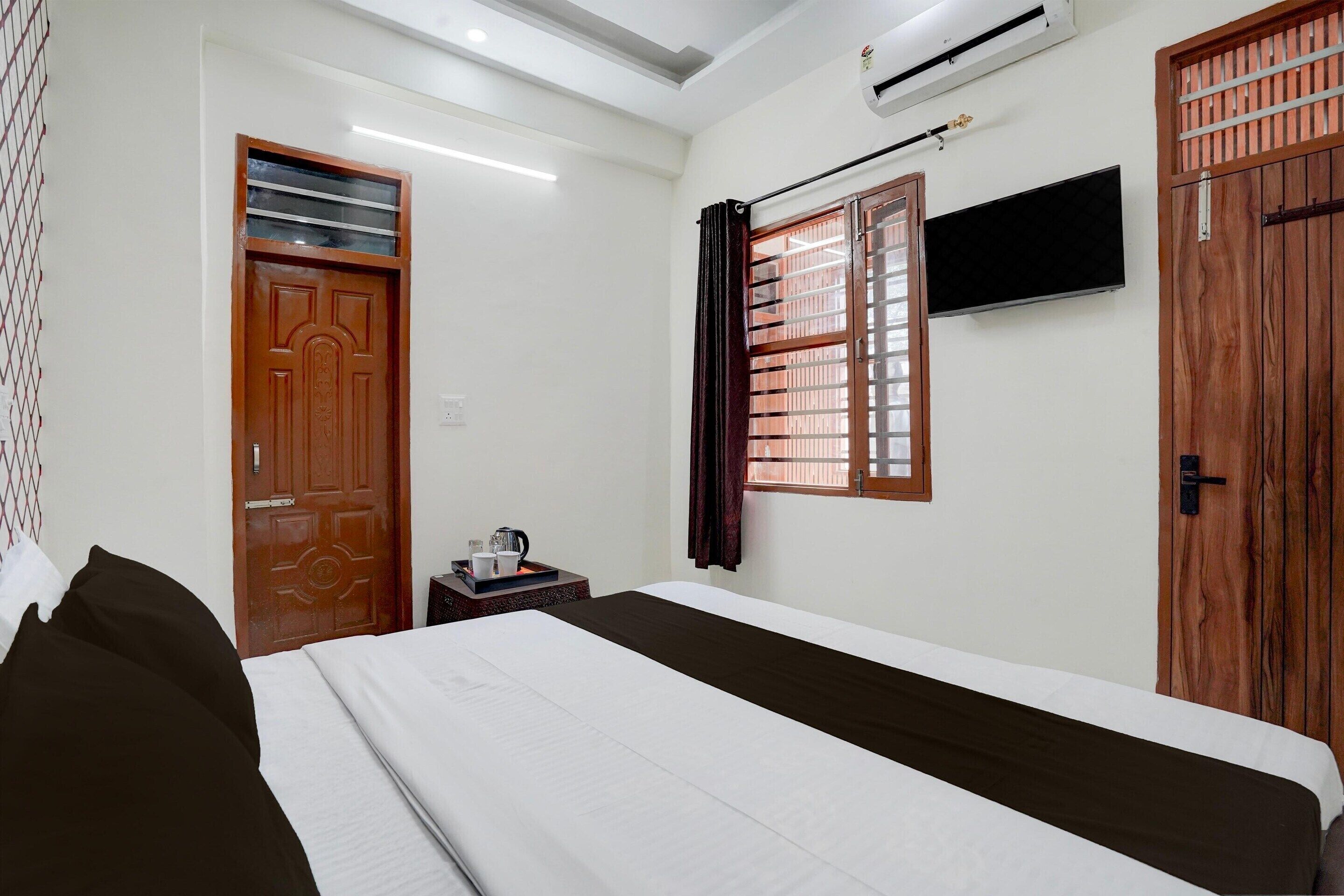 A hotel room with a bed, a TV mounted on the wall, a window with curtains, and a door with a security gate.