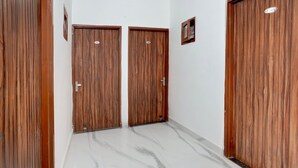 A hallway with two wooden doors, a small framed picture on the wall, and a marble floor. - Deluxe Hotel Holiday Spot (Mohali)