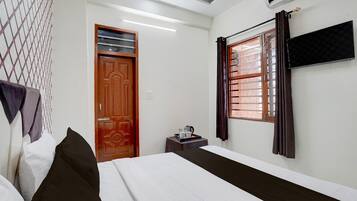 A hotel room with a bed, a small table with a tray, a window with curtains, and a wall-mounted air conditioner.