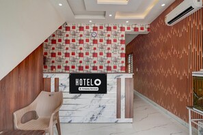 Un comptoir d’accueil d’hôtel avec une enseigne « HOTELO », un mur orné de motifs et un mur composé de lattes de bois.