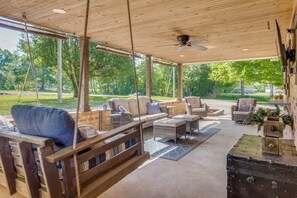 A covered outdoor seating area with wicker furniture, a swing, and a rustic chest. - Covered Patio, Fire Pit & Grills: Olmstead Getaway (Olmstead)