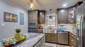 A modern kitchen with wooden cabinets, stainless steel appliances, and a marble countertop. - Covered Patio, Fire Pit & Grills: Olmstead Getaway (Olmstead)