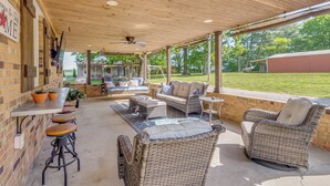 A covered patio area with outdoor furniture, a brick wall, and a view of the surrounding landscape. - Covered Patio, Fire Pit & Grills: Olmstead Getaway (Olmstead)