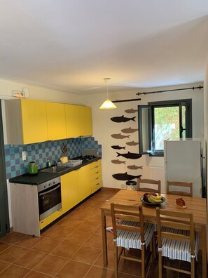 A compact kitchen with yellow cabinets, a tiled backsplash, a dining table with chairs, and a wall decorated with fish cutouts.