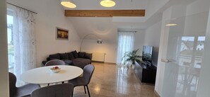 Ein modernes Wohnzimmer mit einer Couch, einem Esstisch mit Stühlen, einem Fernseher und einer Pflanze.