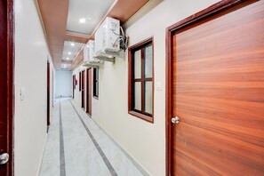 Un pasillo con puertas de madera, unidades de aire acondicionado y suelo de baldosas.
