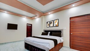 A bedroom with a bed, a wooden door, and three framed pictures on the wall. - Collection O Kanpur Domestic Airport (Kanpur)