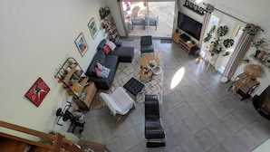 Un grand espace de vie comprenant un canapé, une table basse et un téléviseur, un escalier et un balcon agrémenté de plantes.