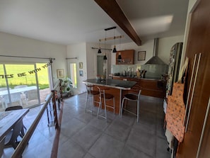 A modern kitchen with a large island, bar stools, and a view to the outside. - Large modern house at the foot of the mountains with swimming pool and 2 Siberian cats (Brié-et-Angonnes)