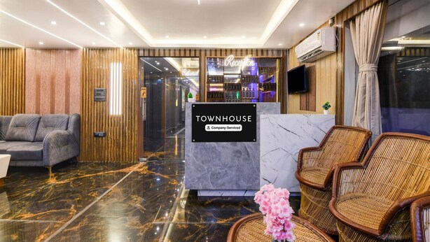 A reception area with a marble floor, a reception desk labeled 'TOWNHOUSE,' a grey sofa, wicker chairs, and a modern chandelier.