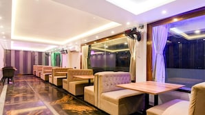 A hotel room with a marble floor, beige seating, a large window with curtains, and a ceiling with recessed lighting.