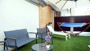 Eine Terrasse mit einer Hängematte, zwei Liegestühlen, einem kleinen Tisch und einem Topfpflanzen.