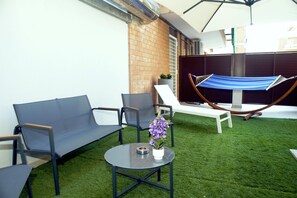 Eine Terrasse mit einer Hängematte, zwei Liegestühlen, einem kleinen Tisch und einem Topfpflanzen.