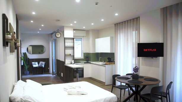Ein Hotelzimmer mit Bett, Schreibtisch, einer kleinen Küchenzeile, Fernseher und Bad.