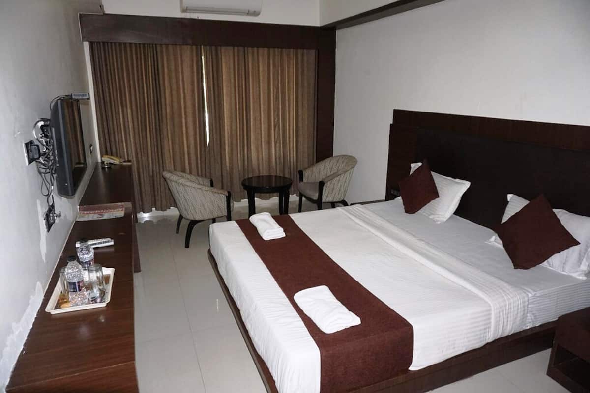 A hotel room with a large bed, a desk with a telephone, a small table, two chairs, and a TV.