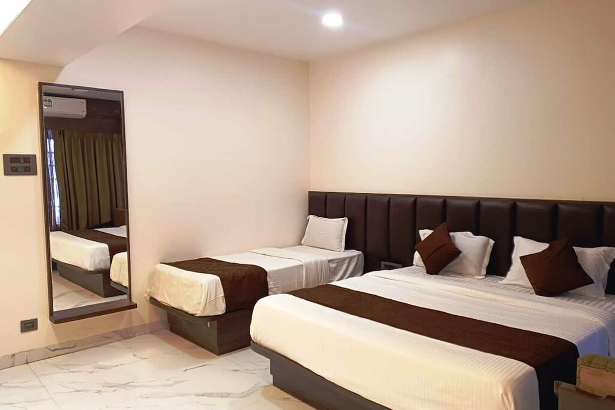 A hotel room with a large bed, two smaller beds, a mirror, and a ceiling light.