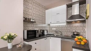 Una cucina moderna con mobili bianchi, un forno a microonde, una macchina per il caffè e una ciotola di frutta sul piano di lavoro.