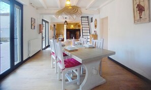 A dining area with a long table, white chairs, and a hanging light fixture. - Cosy house with swimming pool, a trip to Gascony! (Montréal)