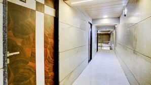 Un pasillo con piso de mármol, una puerta con el símbolo de número y un techo con iluminación empotrada.