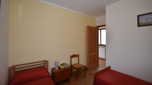 A bedroom with two beds, a wooden chair, a nightstand with a lamp, and a door leading to another room. - In the Peaceful Hillside Village of Aurano (Aurano)