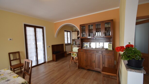 A room with wooden flooring, a dining table, chairs, a kitchen area with cabinets, and a potted plant. - In the Peaceful Hillside Village of Aurano (Aurano)