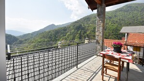 A balcony with a view of a mountainous landscape, a table with a potted plant, and a chair. - In the Peaceful Hillside Village of Aurano (Aurano)