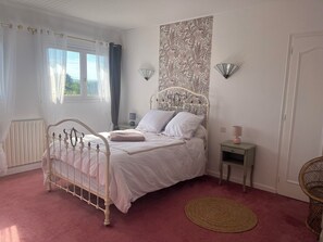 Une chambre à coucher avec un lit blanc, une table de chevet avec une lampe, une tapisserie murale et une fenêtre avec des rideaux.
