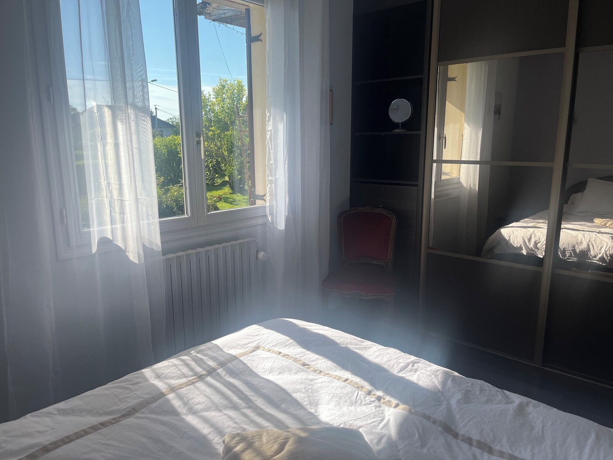 Une chambre à coucher avec un lit, une chaise, un radiateur et une fenêtre avec des rideaux.