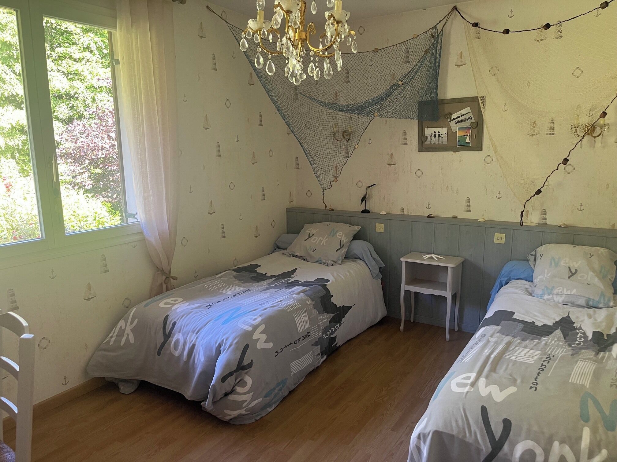 Une chambre avec deux lits, un lustre, une petite table et une fenêtre avec des rideaux.