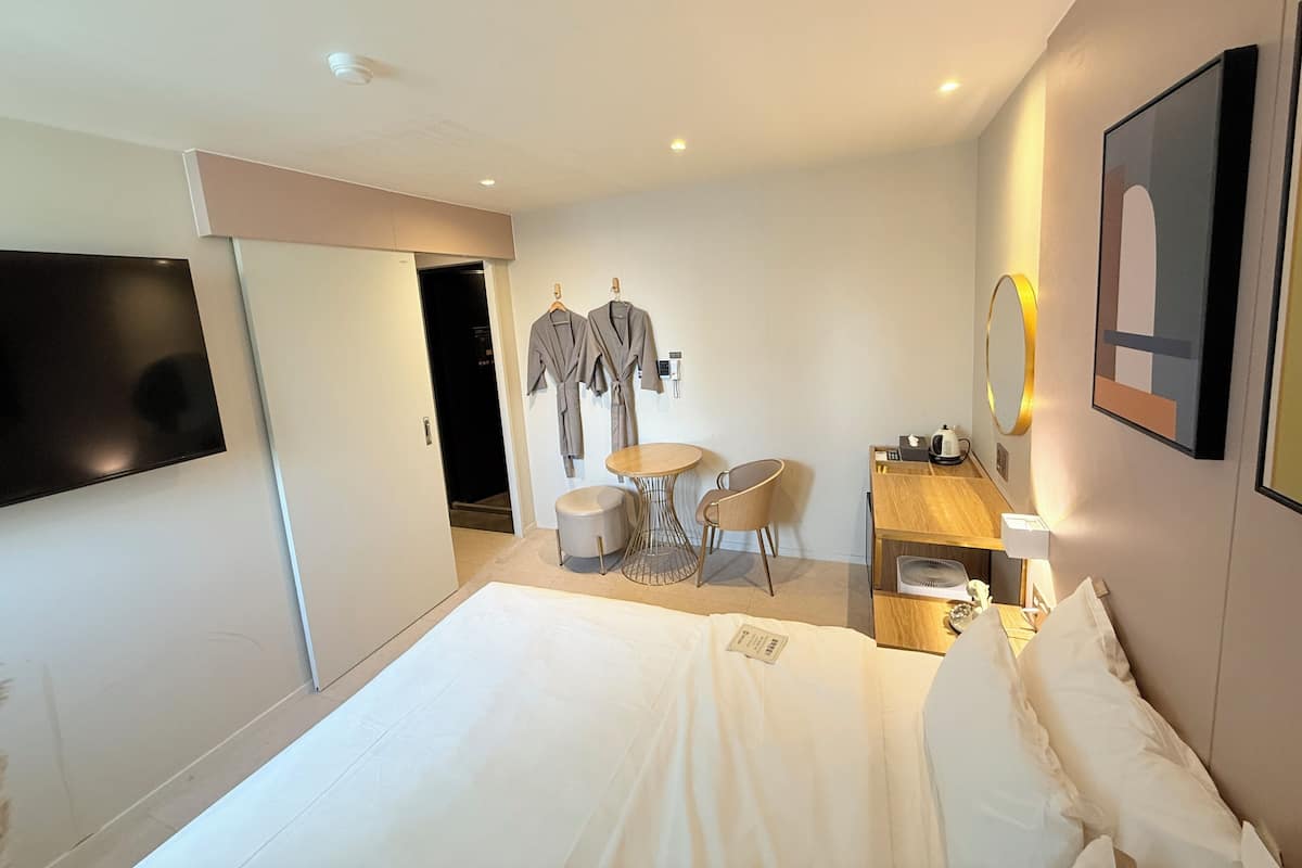 A hotel room with a bed, a TV, a desk with a chair, a small table, and a mirror.