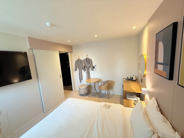 A hotel room with a bed, a TV, a desk with a chair, a small table, and a mirror.