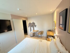 A hotel room with a bed, a TV, a desk with a chair, a small table, and a mirror.