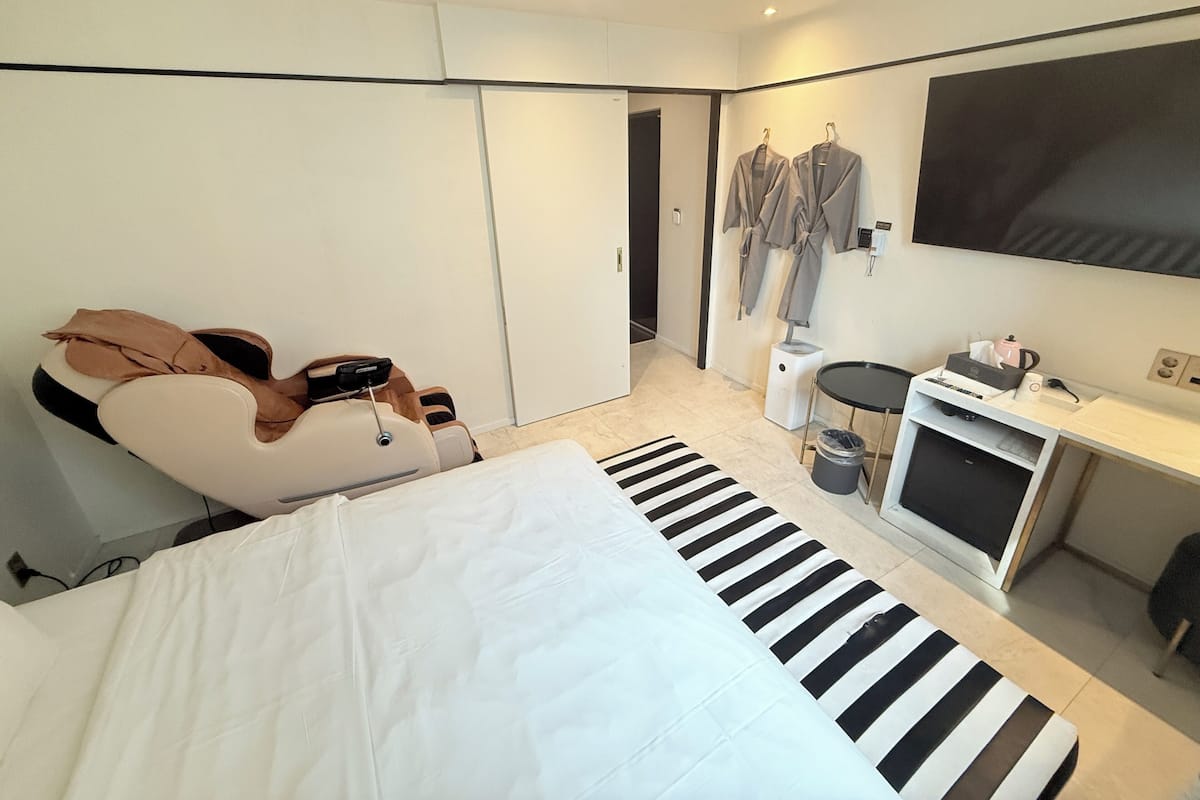 A modern hotel room with a bed, a massage chair, a TV, and a desk with a computer and other amenities.