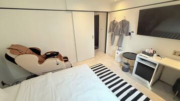 A modern hotel room with a bed, a massage chair, a TV, and a desk with a computer and other amenities.