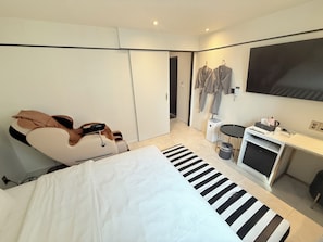 A modern hotel room with a bed, a massage chair, a TV, and a desk with a computer and other amenities.